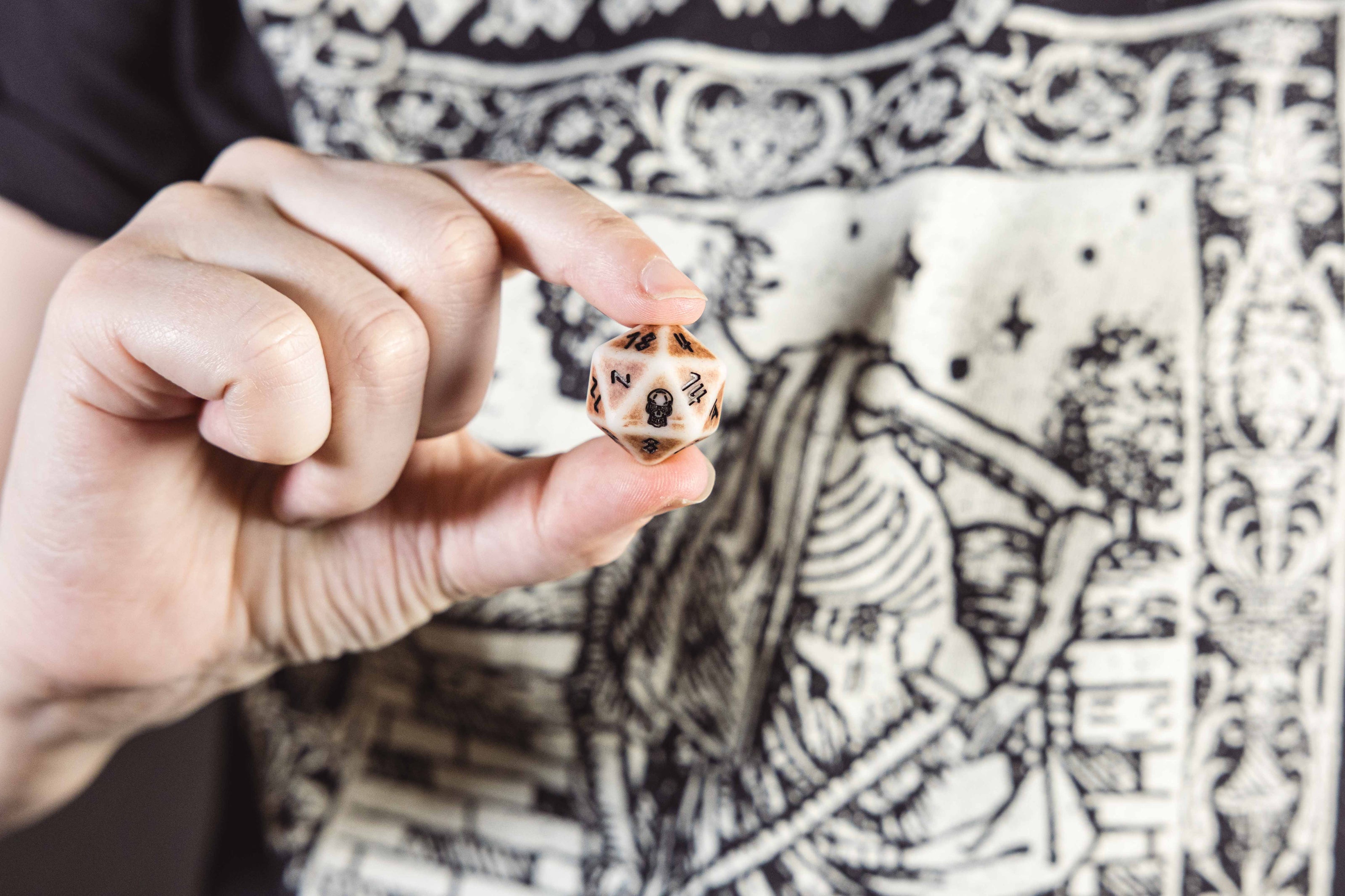 A hand holding a D20 showing the skull icon representing the '20' face