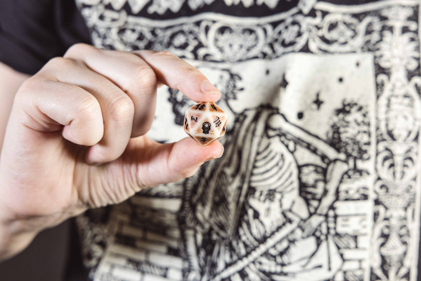 A hand holding a D20 showing the skull icon representing the '20' face